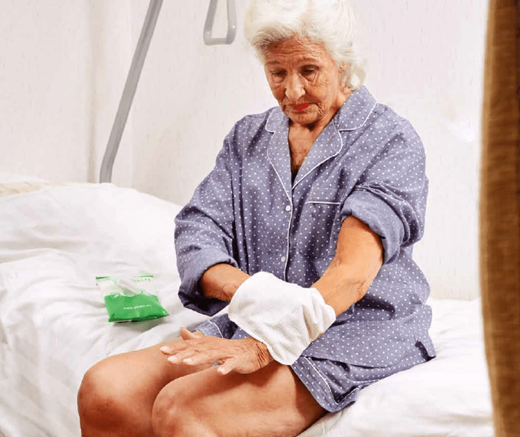 An eldery woman doing a bed bath with a washing without water glove